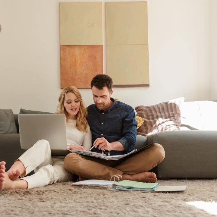 Couple sitting on the floor going over paperwork while using a laptop