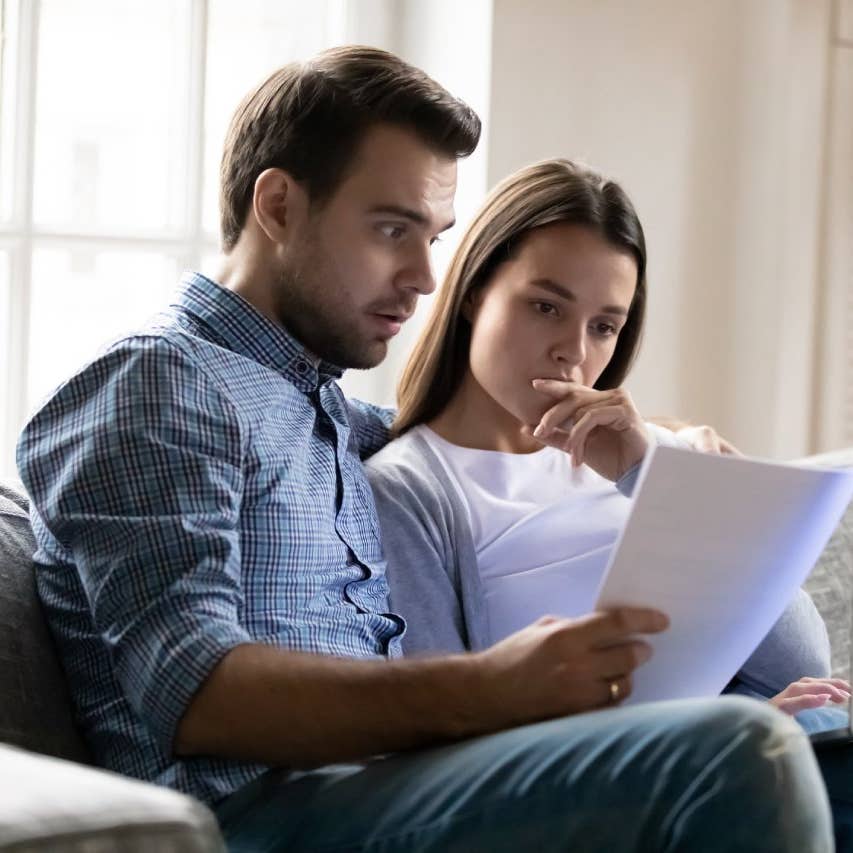 Shocked worried young couple reading documents, financial problems, using laptop, online banking service, checking mortgage or insurance contract terms, calculating domestic bills or taxes