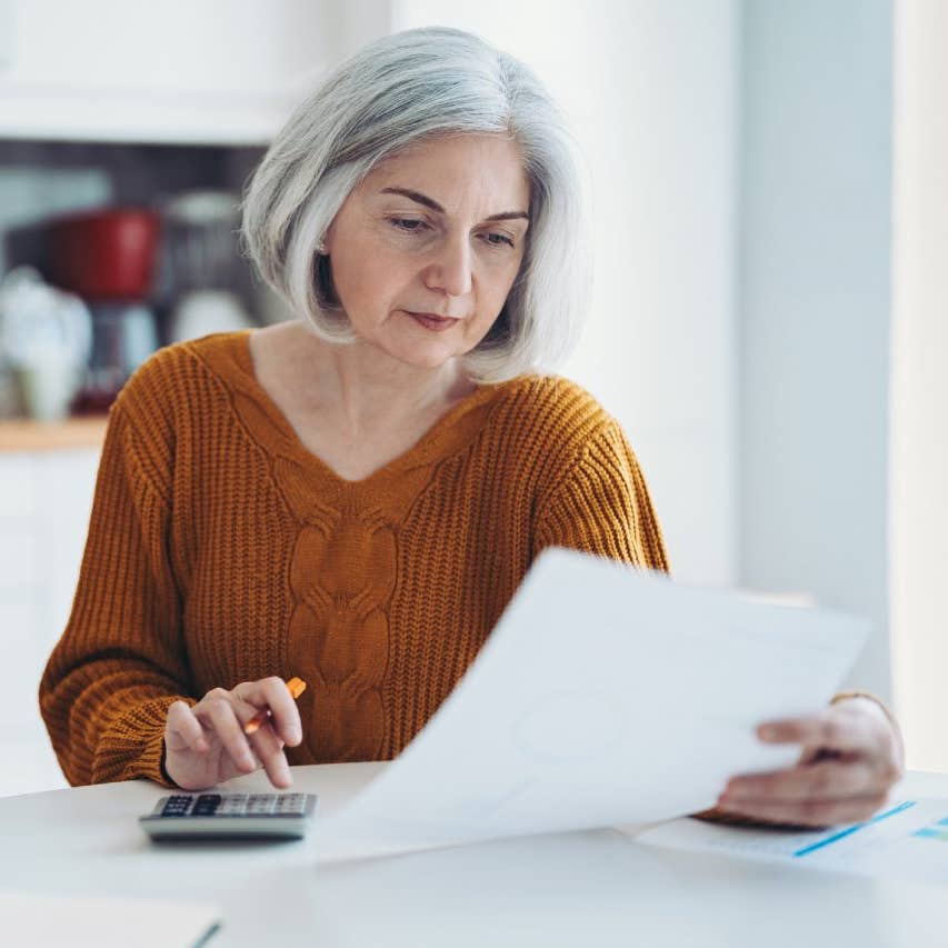 Mature woman with calculator, notebook and documents at home
