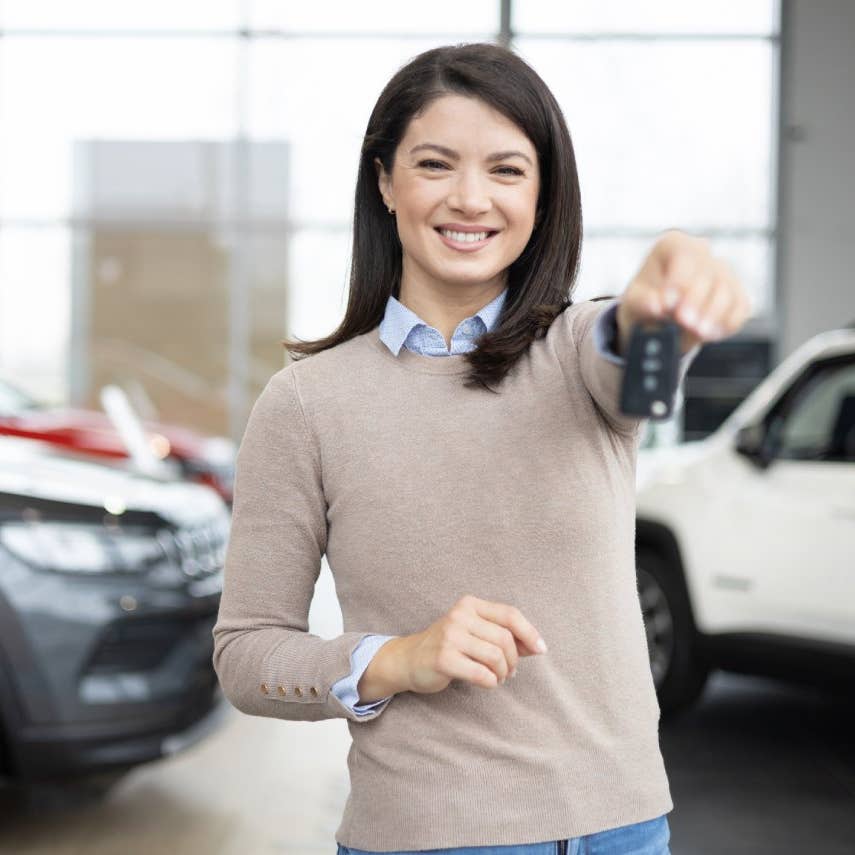 Woman points car key to camera in auto showroom